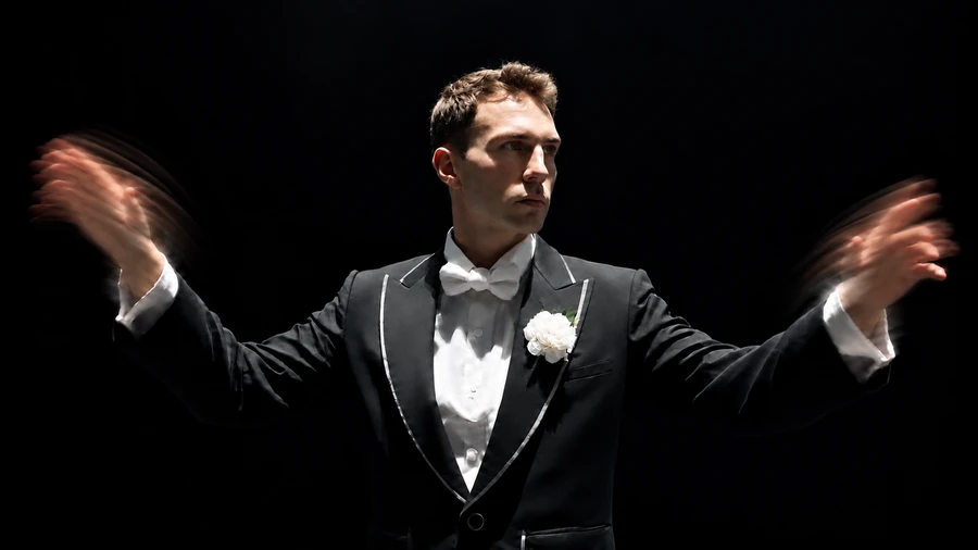 Gabriel Wyatt in a tuxedo, conducting with expressive motion in both hands.